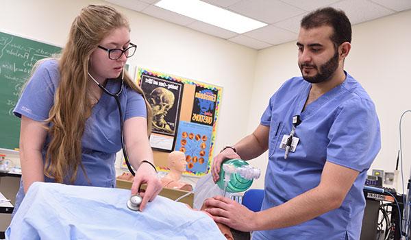 Two nursing students work together in a lab to assist a patient.